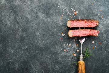 Steaks T-bone. Slices of beef grilled meat barbecue steak on meat fork on burned dark wooden background with copy space for your text. Top view. Mock up.