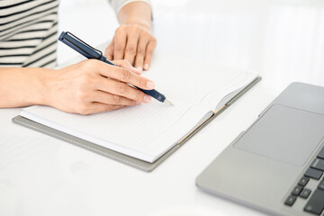 Asian businesswoman in casual clothes writing notes in notepad while working on laptop , close up clean image in front of the window in soft light..