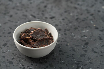 spiced beef jerky in white bowl on terrazzo countertop