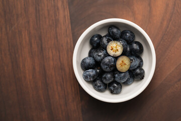 Top view of ripe blueberries in a white bowl on wood table