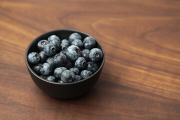 Big organic blueberries in a black bowl on walnut table