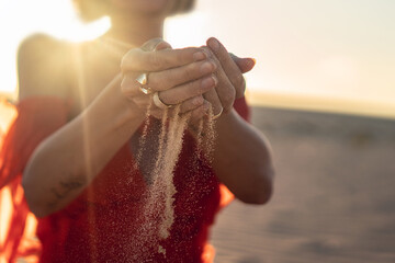 Elegant woman with sand falling through her hands on the beach at sunset time. Golden light.