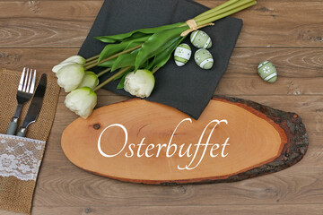 Der Text Osterbuffet auf eine Holzscheibe geschrieben mit Besteck, Blumen und Ostereiern. 