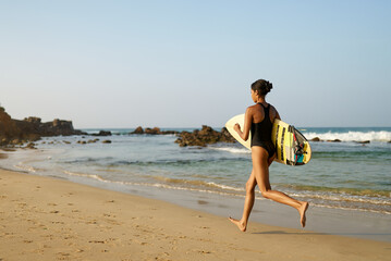 African american woman running with surfboard on ocean beach. Black female surfer with surf board....