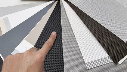 drapery catalog samples palette. architect's hand choosing samples of roller blind fabrics in...