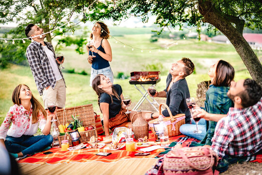 Fancy people laughing at vineyard place after sunset - Food and beverage concept with men and women drinking wine at barbeque party - Happy friends camping at open air pic nic on warm vivid filter