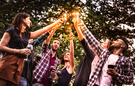 Fancy millenial people having fun with fire sparkles and toasting wine - Young trendy friends cheering at picnic barbecue party on night mood out side - Youth life style concept on warm dark filter