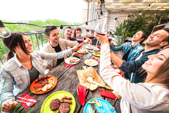 Wide angle view of fancy people toasting red wine together at pic nic party in open air villa - Happy friends eating bar-b-q food at house patio - Trendy life style concept on bright vivid filter