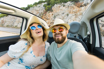 Happy beautiful couple in love taking a selfie portrait driving a convertible car on the road at vacation. Rental cars and vacation