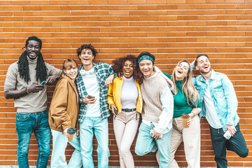 Multiracial young people smiling at camera standing in front of a wall background - Youth community concept with guys and girls hugging together - University students outside school