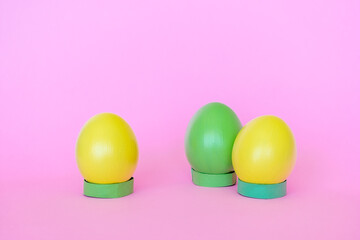 Obraz na płótnie Canvas Easter eggs in a vertical position of yellow and green on a pink background.