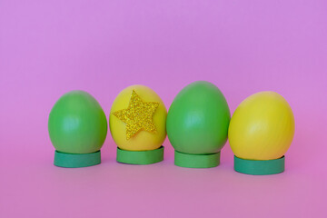 Easter eggs in yellow and green in a vertical position, decorated with a star on a pink background.