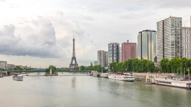 The Eiffel Tower and the Statue of Liberty reflected on water with modern buildings and traffic on road timelapse hyperlapse. View from Mirabeau bridge before sunset. Paris, France