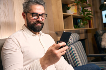 Cheerful man reading something on his mobile phone