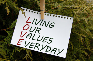 LIVING OUR VALUES EVERYDAY - words on white paper with clothespin on a green background of branches