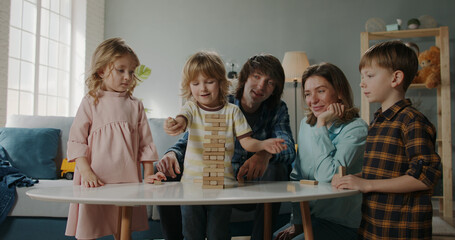 Three little caucasian kids playing with their parents, constructing a wooden blocks tower in board game. Happy positive family spending time together at home 