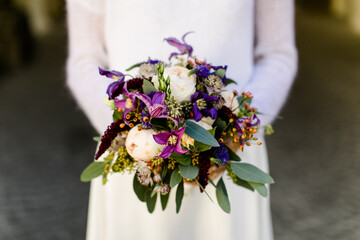 Braut mit langen Ärmeln hält lila Brautstrauss