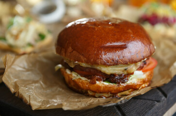 Big juicy cheeseburger served on decorative parchment paper and wooden board in a restaurant. Large beef burger prepared for lunch in a diner