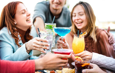 Young friends toasting multicolored fruit drinks - Fancy people having fun together drinking cocktails at happy hour - Food and beverage life style concept on vivid filter with shallow depth of field