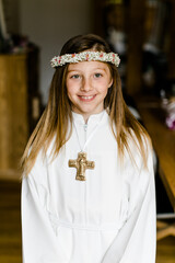 Hübsches junges Mädchen im weißen Kleid mit Blumenkranz bei Erstkommunion