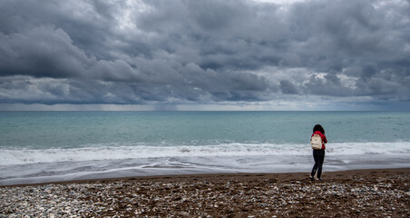 Fototapeta na wymiar One woman standing on the beach. Stormy sky windy waves. Paphos Cyprus