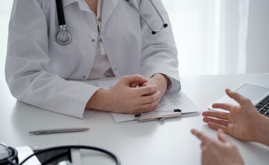 Doctor and patient discussing current health questions while sitting at the desk in clinic office, closeup. Medicine and healthcare concept