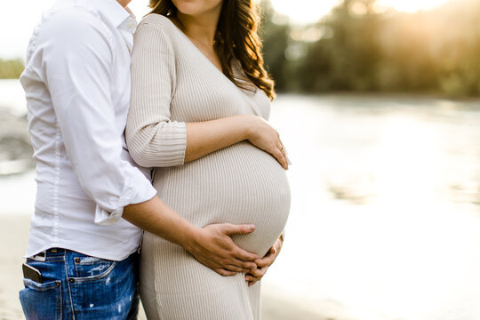 Mutter und Vater halten Babybauch w&auml;hrend Sonnenuntergang