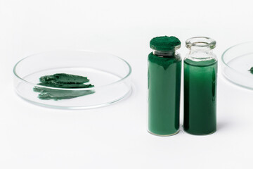 Spirulina powder in a jar. A solution or oil from spirulina in a jar. On a white background. Petri dishes with maxa or spirulina cream.