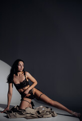 Fototapeta na wymiar Young sexy woman poses sitting in black lacy lingerie in BDSM style.
