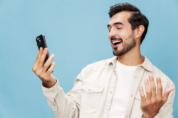 Portrait of a brunette man talking on the phone mobile and internet online, smile with teeth surprise and happiness, on a blue background in a white T-shirt, copy space
