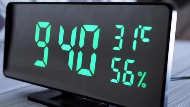 Digital Clock Showing Time on Green Display 9:40 AM, Temperature, Air Humidity. Modern mirror clock, alarm clock with a thermometer, hydrometer standing on a desk on white background. Time concept.