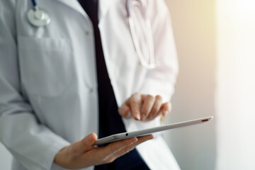 Doctor woman using tablet computer while standing near panorama window in clinic, close up. Physician or surgeon at work. Medicine concept