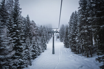 Ski lift transports skiers and snowboarders in foggy day at snowy mountain. Frozen funicular. Pinzolo and Madonna di Campiglio ski resort. January 2023