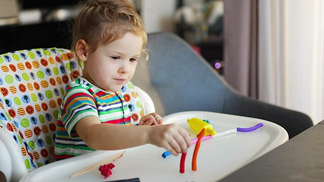 Little girl plays with multi-colored plasticine, creates different shapes