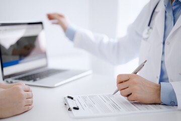 Doctor and patient discussing something and using laptop while sitting opposite each other at the desk in clinic office. Perfect medical service and medicine concept