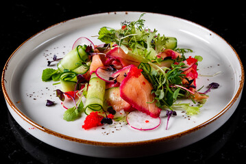Green salad with salmon, cucumbers, lettuce, spices, caviar in plate