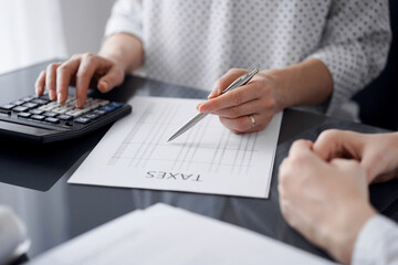 Woman accountant using a calculator and laptop computer while counting taxes for a client. Business audit and finance concepts