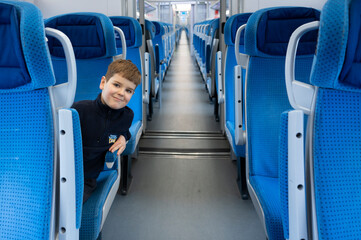 Child in cabin of a modern passenger train. Empty blue seats inside train cabin, corridor view....
