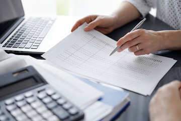 Female accountant pointing with a pen into audit paper while explaining tax counting results, close...
