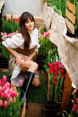 A model among tulips at a spring photo shoot. Modern clothes of a farmer. Ukrainian girls are very beautiful. Long hair