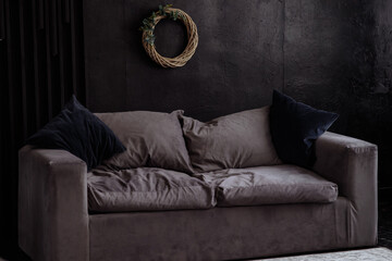 Gray velor sofa in a dark room against a black wall. Interior loft with concrete walls.