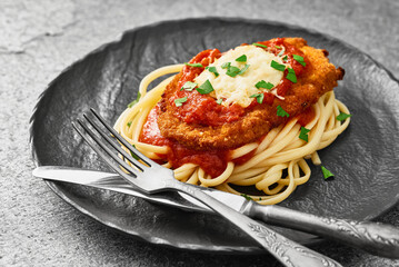 Close-up of a plate of homemade Chicken Parmesan with spaghetti on a gray stone background. Low...