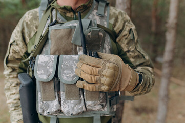 a military man in a camouflage uniform and tactical gloves holds a walkie-talkie.