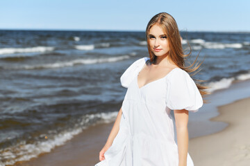 Fototapeta na wymiar Happy, beautiful woman on the ocean beach standing in a white summer dress. Portrait