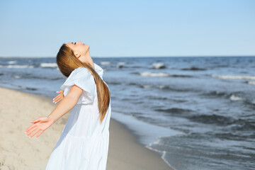 Fototapeta na wymiar Happy, beautiful woman on the ocean beach standing in a white summer dress, open arms