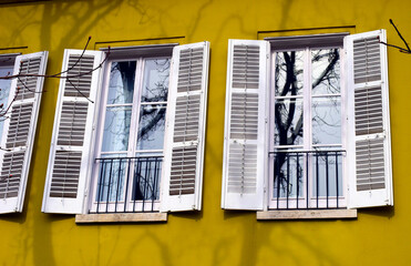 yellow stucco home exterior facade detail. small french balcony and glass door. home ownership concept. horizontal steel balustrade with metal bar pickets. abstract view. open white palette shutters