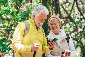 Cheerful caucasian senior couple with backpack and walking sticks hike in the forest while using mobile phone, elderly couple enjoying healthy lifestyle and retirement