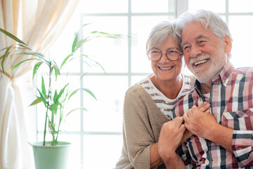 Happy senior couple embracing and laughing sitting at home. Modern retirees laugh at something funny, expressing happiness and carefree