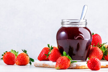 Strawberry jam in glass jar and fresh berries, white table background, copy space
