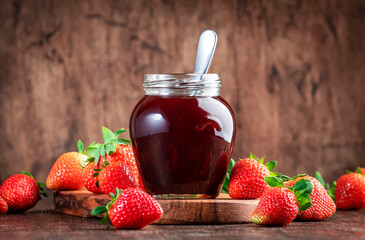 Strawberry jam in glass jar and fresh berries, rustic wooden table background, copy space
